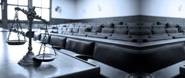 Una balanza metálica de la justicia reposa sobre una mesa frente a filas de bancos vacíos en la sala del tribunal.