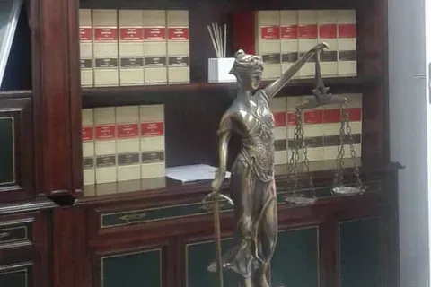 Una estatua de bronce de la Dama de la Justicia se alza frente a una estantería de madera oscura repleta de filas de libros de leyes.