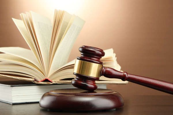 Un mazo de juez de madera oscura descansa sobre su base frente a un libro abierto sobre un fondo marrón.