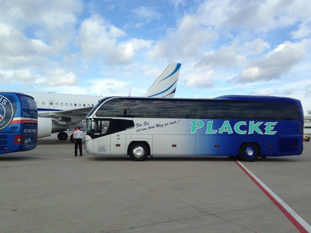 Ein blau-weißer Placke-Bus steht neben einem Flugzeug
