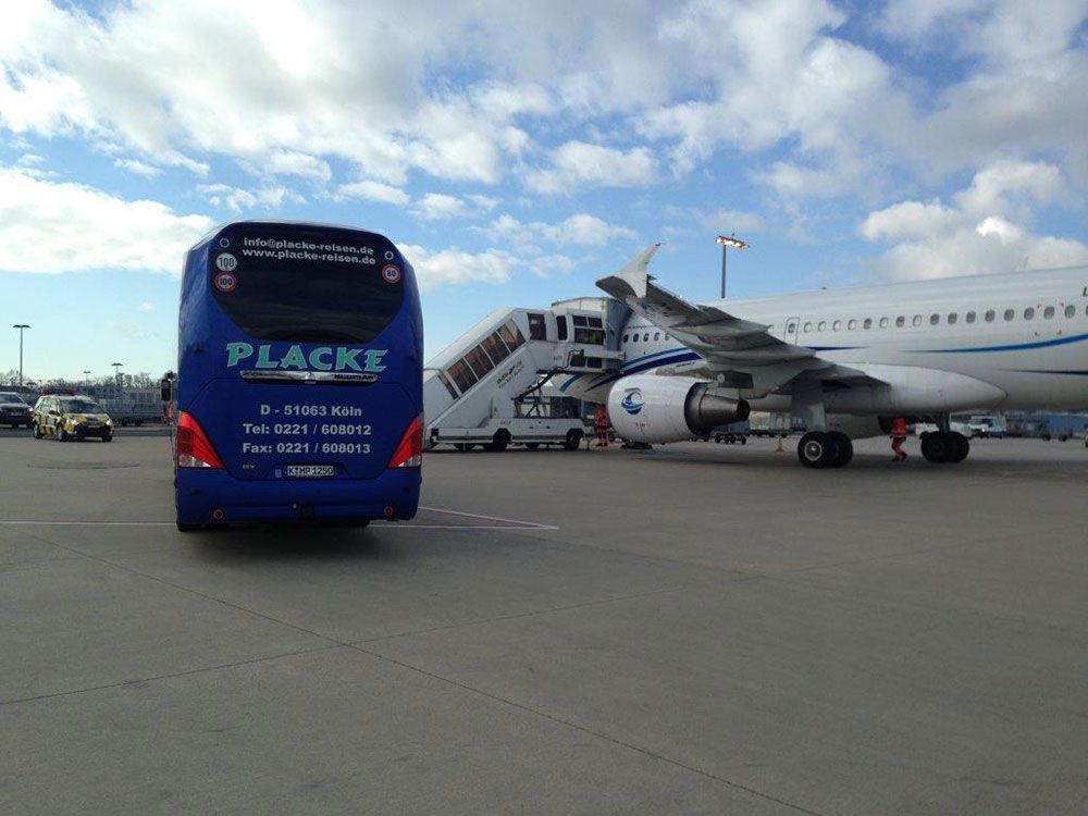 Ein blauer Placke-Bus steht neben einem Flugzeug