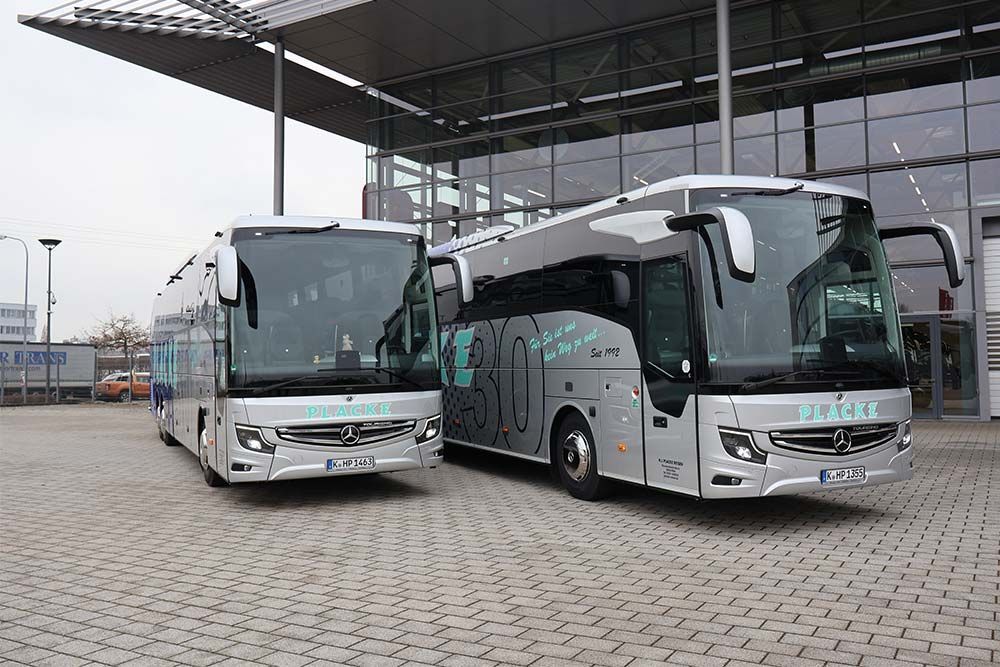 Zwei silberne Busse stehen vor einem Gebäude