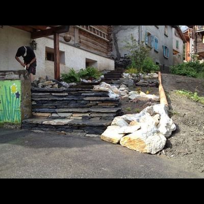 Un homme travaille sur un mur de pierre devant un bâtiment.