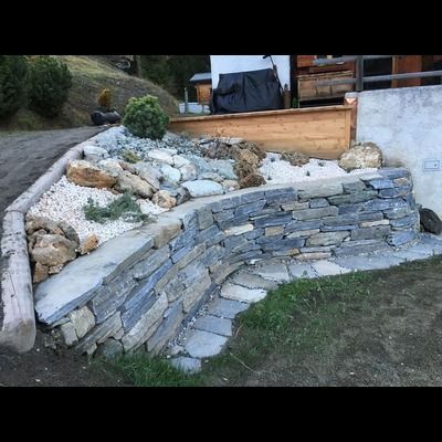 Un mur de pierre est entouré de rochers et de gravier dans une cour.