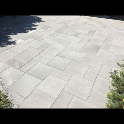 Une allée en béton avec un motif géométrique et un arbre en arrière-plan.