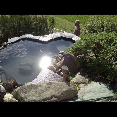 Un homme se tient debout à côté d'un grand étang entouré de rochers.