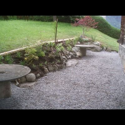 Un chemin de gravier avec une table et des bancs dans un jardin.