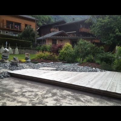 Un pont en bois sur une rivière dans un jardin avec une maison en arrière-plan.