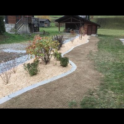 Un jardin avec un chemin et un cabanon en arrière plan.