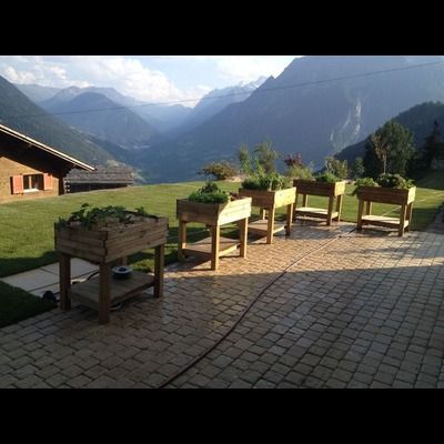 Une rangée de jardinières en bois sur un patio avec des montagnes en arrière-plan.