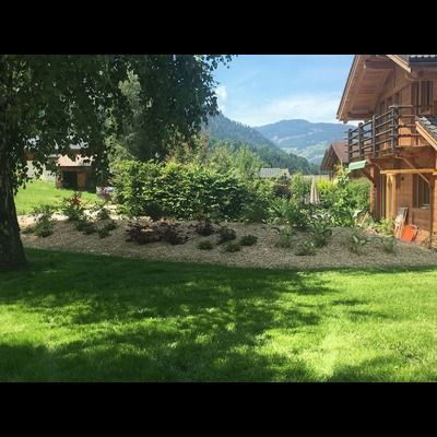 Une grande pelouse verte luxuriante devant une maison en bois avec des montagnes en arrière-plan.
