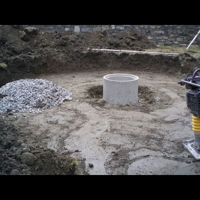 Un puits en béton est en train d'être construit dans la terre à côté d'un tas de gravier.