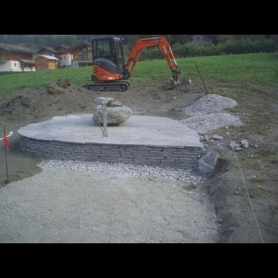 Une petite excavatrice creuse un trou dans le sol à côté d'un mur de pierre.