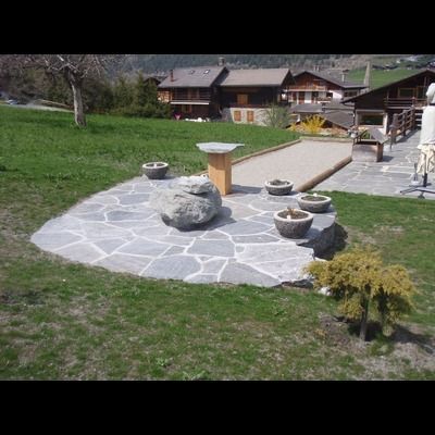 Un patio en pierre avec des plantes en pot et une table au milieu d'un champ herbeux.