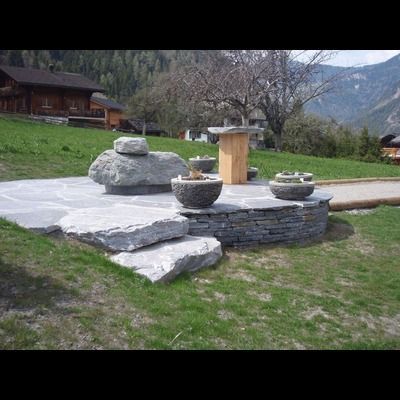 Un patio en pierre avec des marches et des plantes en pot dans un champ herbeux avec des montagnes en arrière-plan.