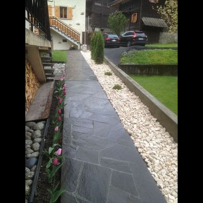 Une allée en pierre entourée de rochers et de fleurs menant à une maison.