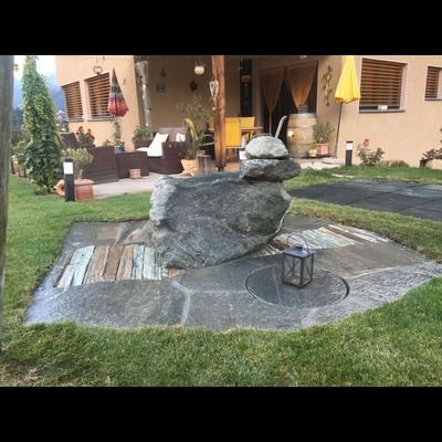 Un gros rocher se trouve au milieu d'une pelouse devant une maison.