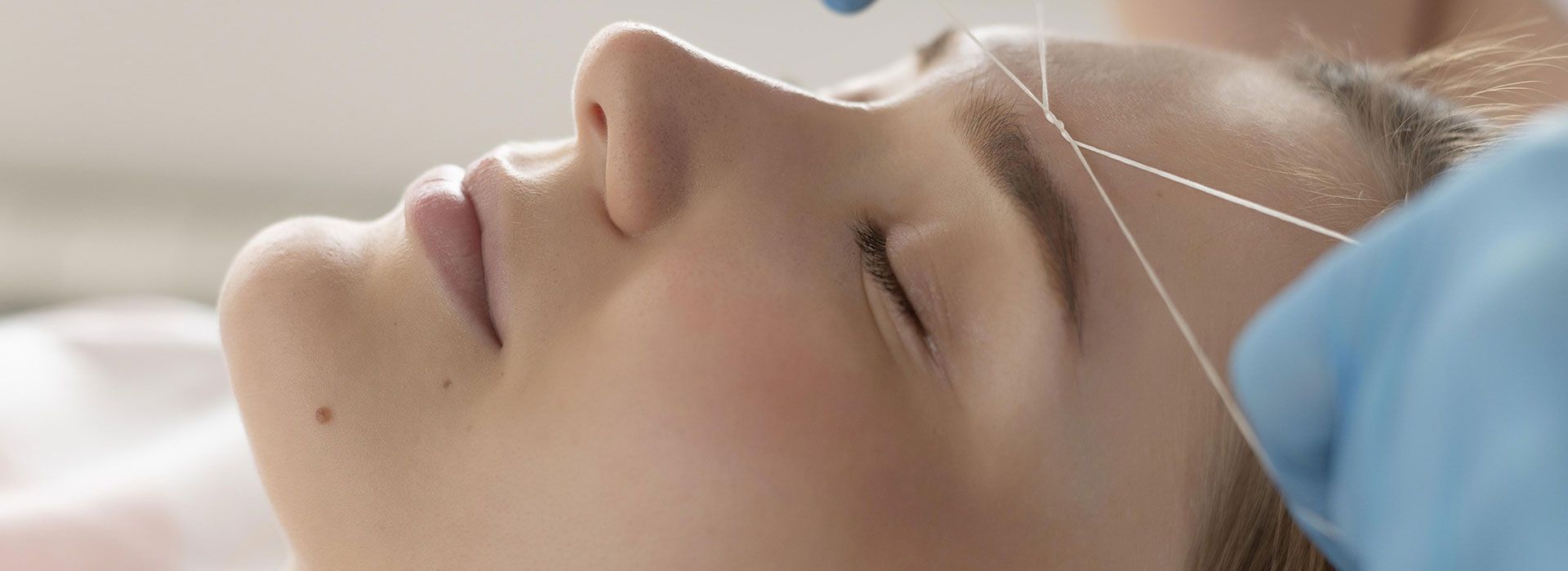 Una mujer se está depilando las cejas con hilo en un salón de belleza.