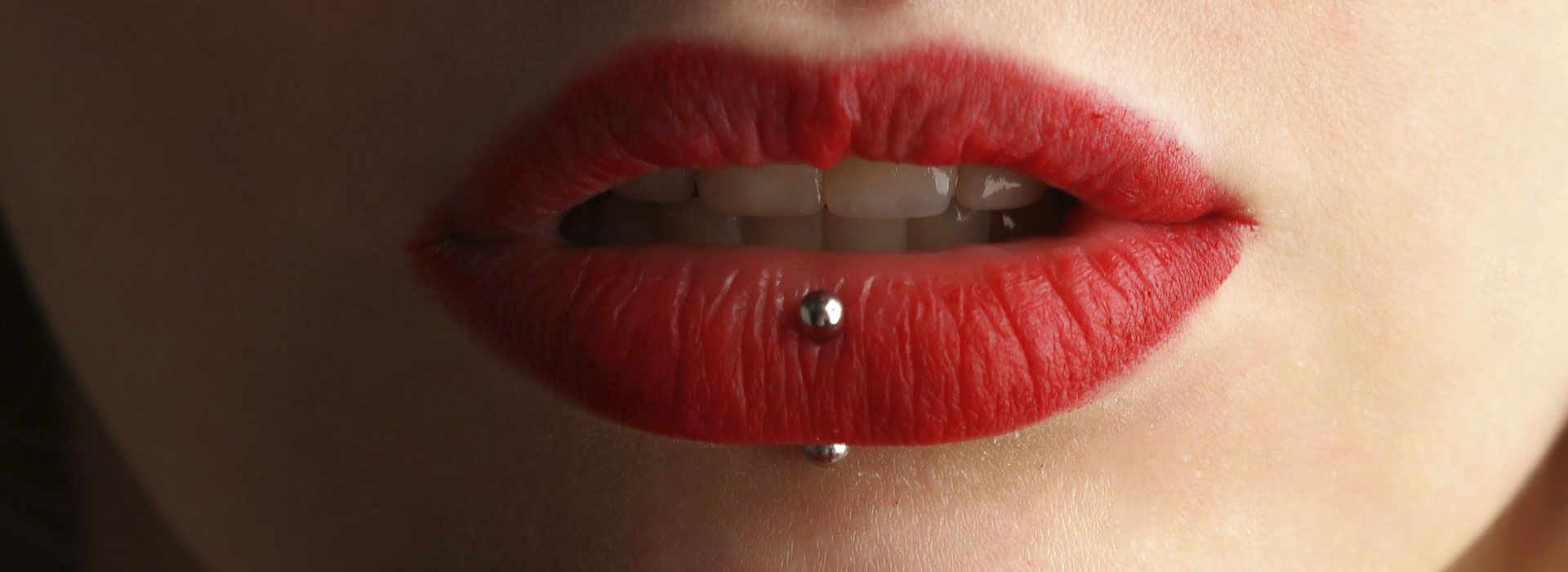 Un primer plano de los labios de una mujer con lápiz labial rojo y un piercing en el labio.