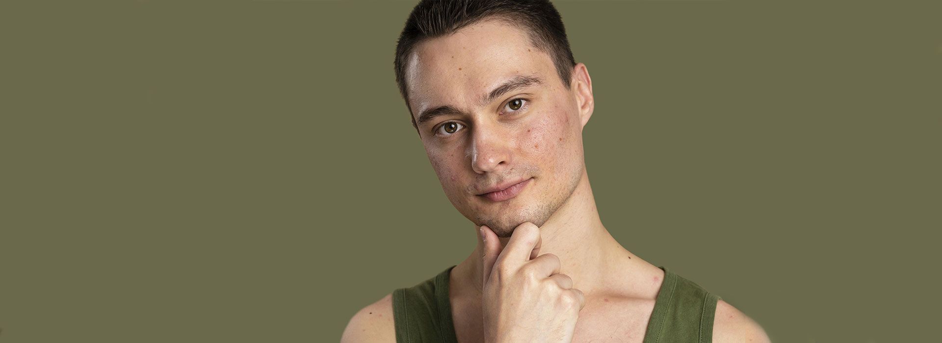 Un joven con una camiseta verde se lleva la mano a la barbilla.