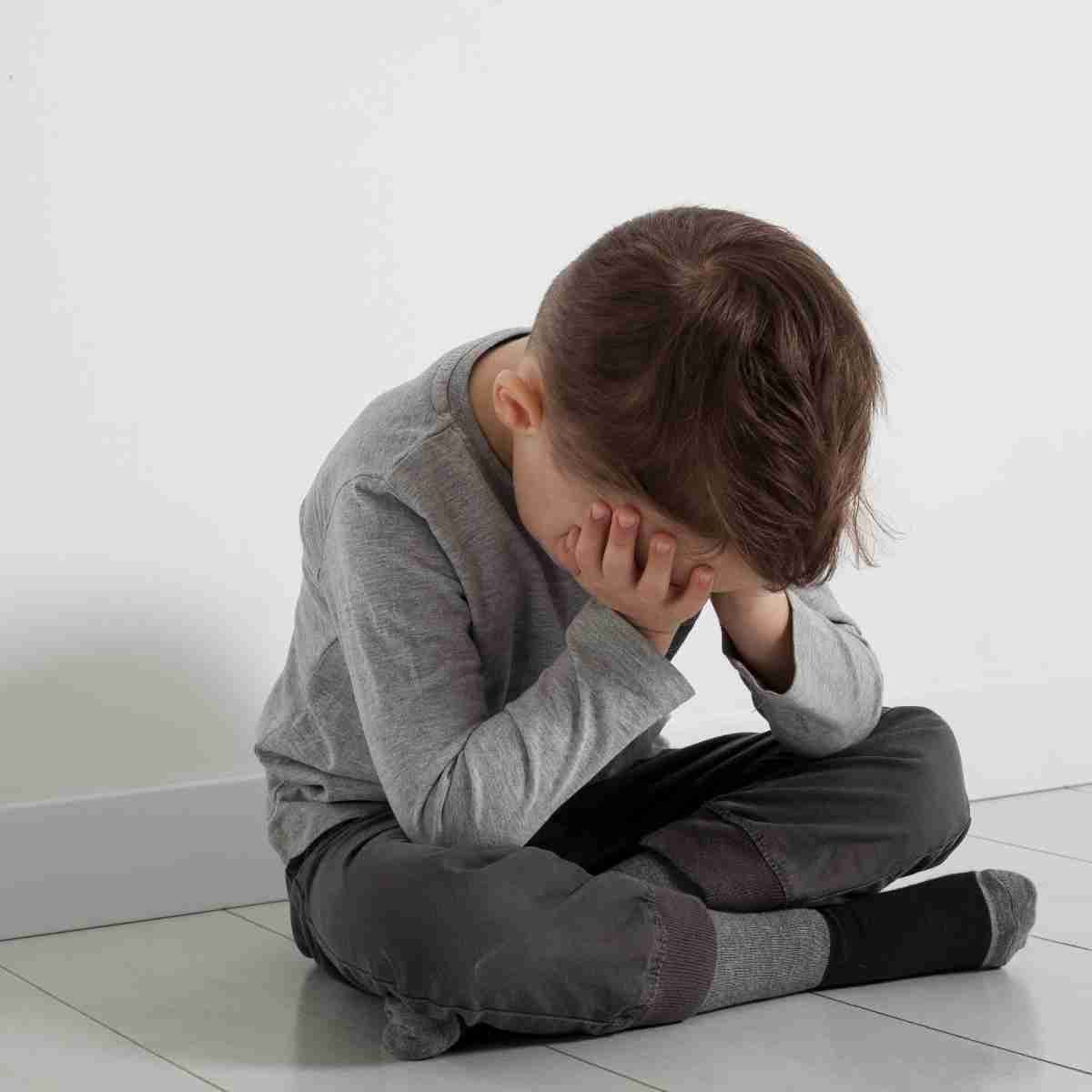 Un niño pequeño está sentado en el suelo con la cabeza entre las manos.