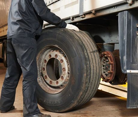 Persona vestida de negro inspeccionando un neumático de camión semirremolque dañado en un garaje.