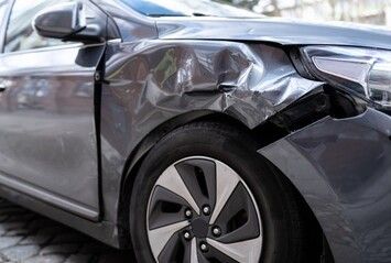 Schwer beschädigte Frontpartie eines silbernen Autos nach einem Zusammenstoß, Motorhaube und Kotflügel verbeult.