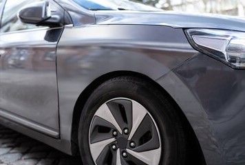 Nahaufnahme der Vorderseite und des Rades eines im Freien geparkten grauen Autos.