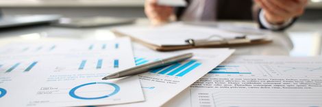 Hände, die mit einem Stift auf einem Schreibtisch Finanzdiagramme und -berichte prüfen