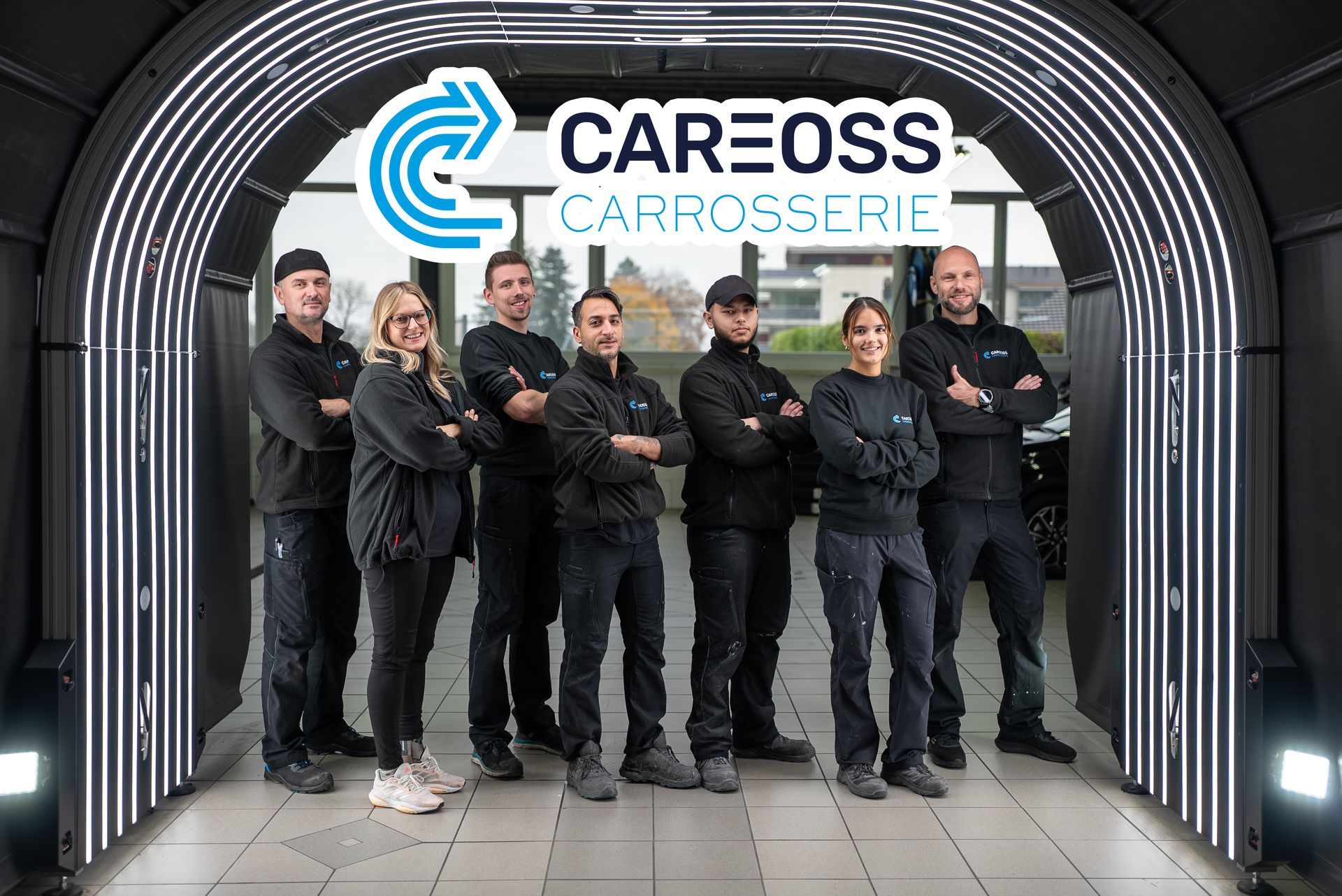 Sechs Mechaniker in schwarzen Arbeitskleidung stehen unter einem Schild der Firma Careoss Carrosserie in einer Garageneinfahrt.