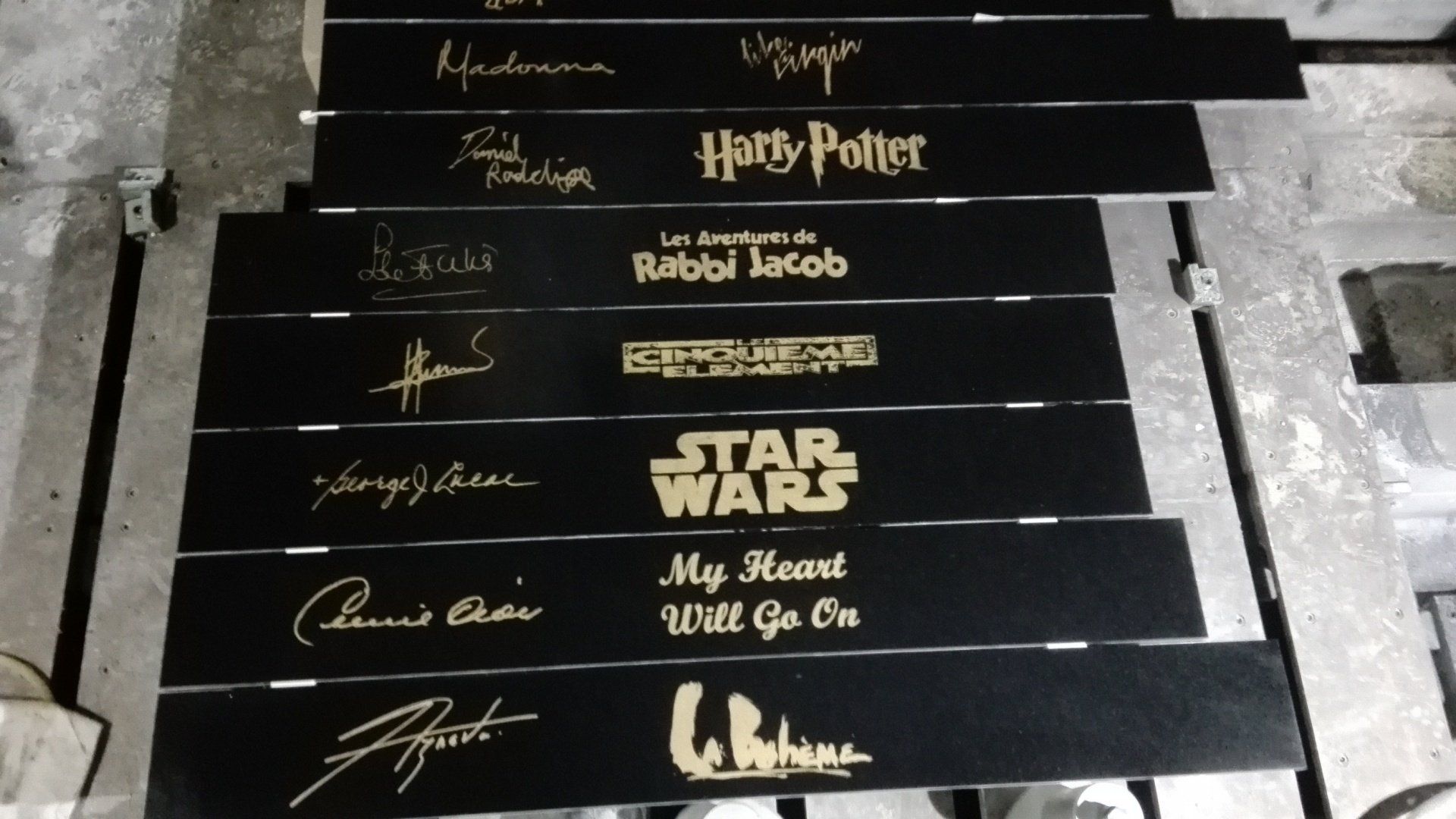 Ensemble de plaques en marbre noir avec des titres de films ou chansons issus de la pop culture en doré