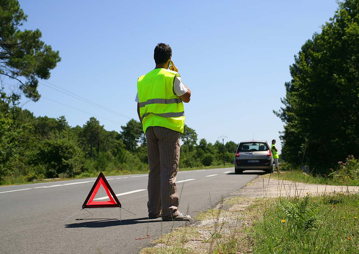 Un homme portant un gilet jaune appelle une assistance au bord de la route