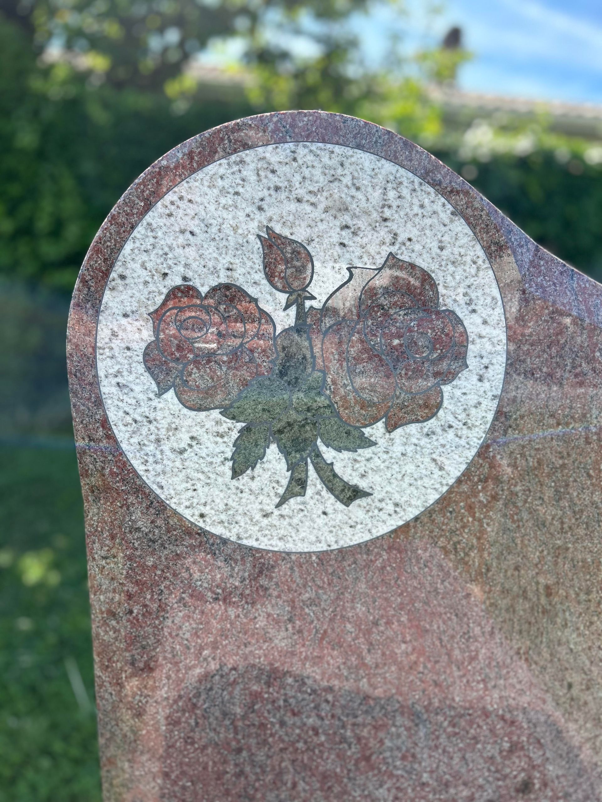 Pierre tombale en granit ornée d'une croix dorée et de motifs floraux.