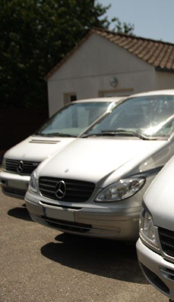 Des fourgonnettes Mercedes argentées garées devant un bâtiment blanc par une journée ensoleillée.