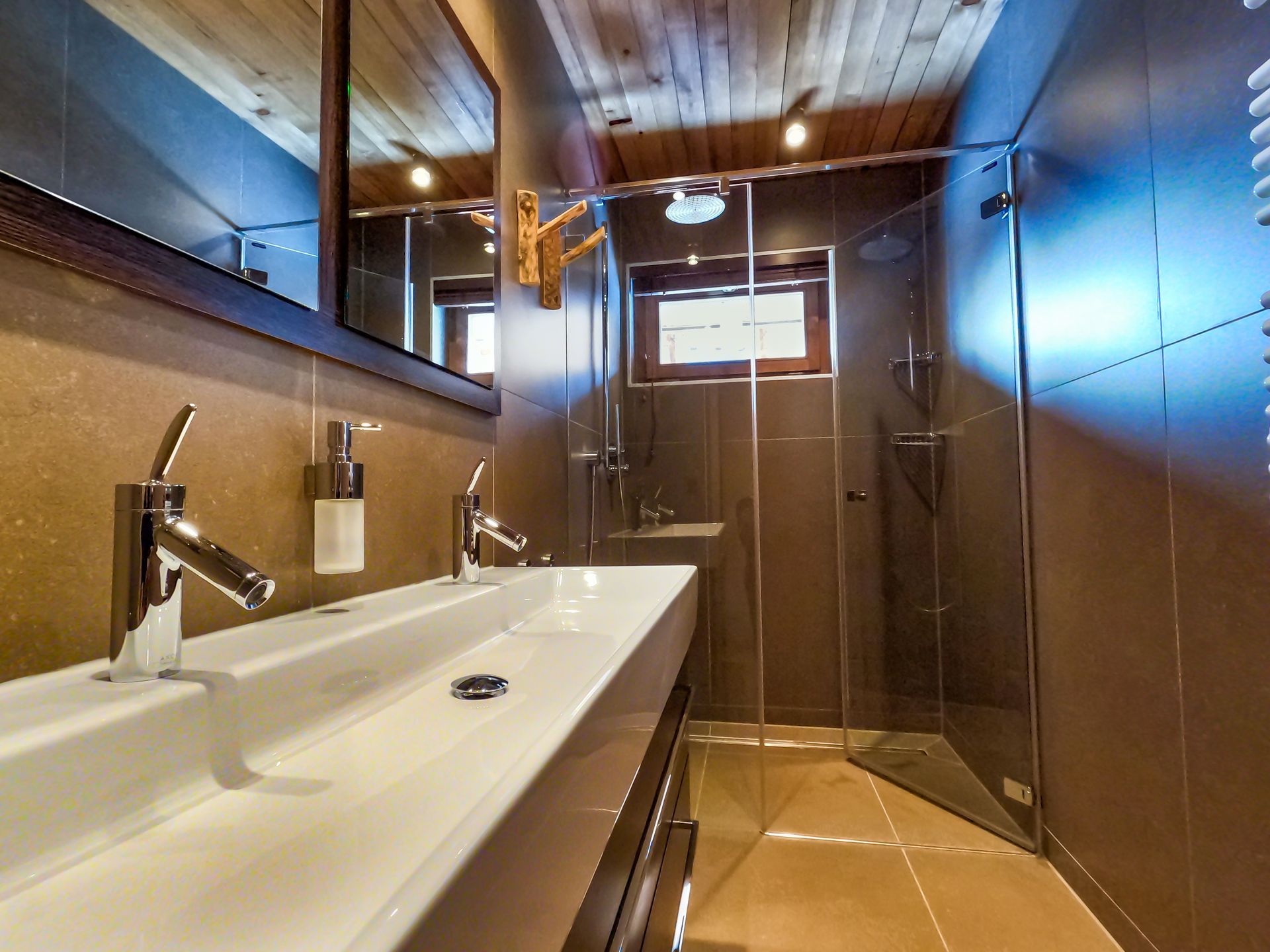 Modernes Badezimmer mit langem weißen Waschbecken, Glasdusche und Holzdecke.