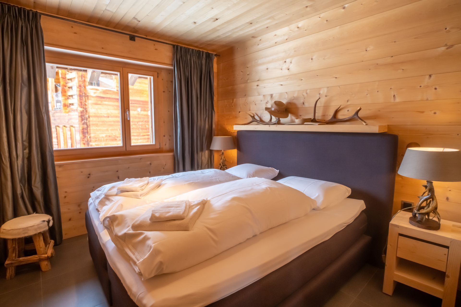 Gemütliches Schlafzimmer mit Holzwänden, einem Doppelbett mit weißer Bettwäsche und einem kleinen Fenster.