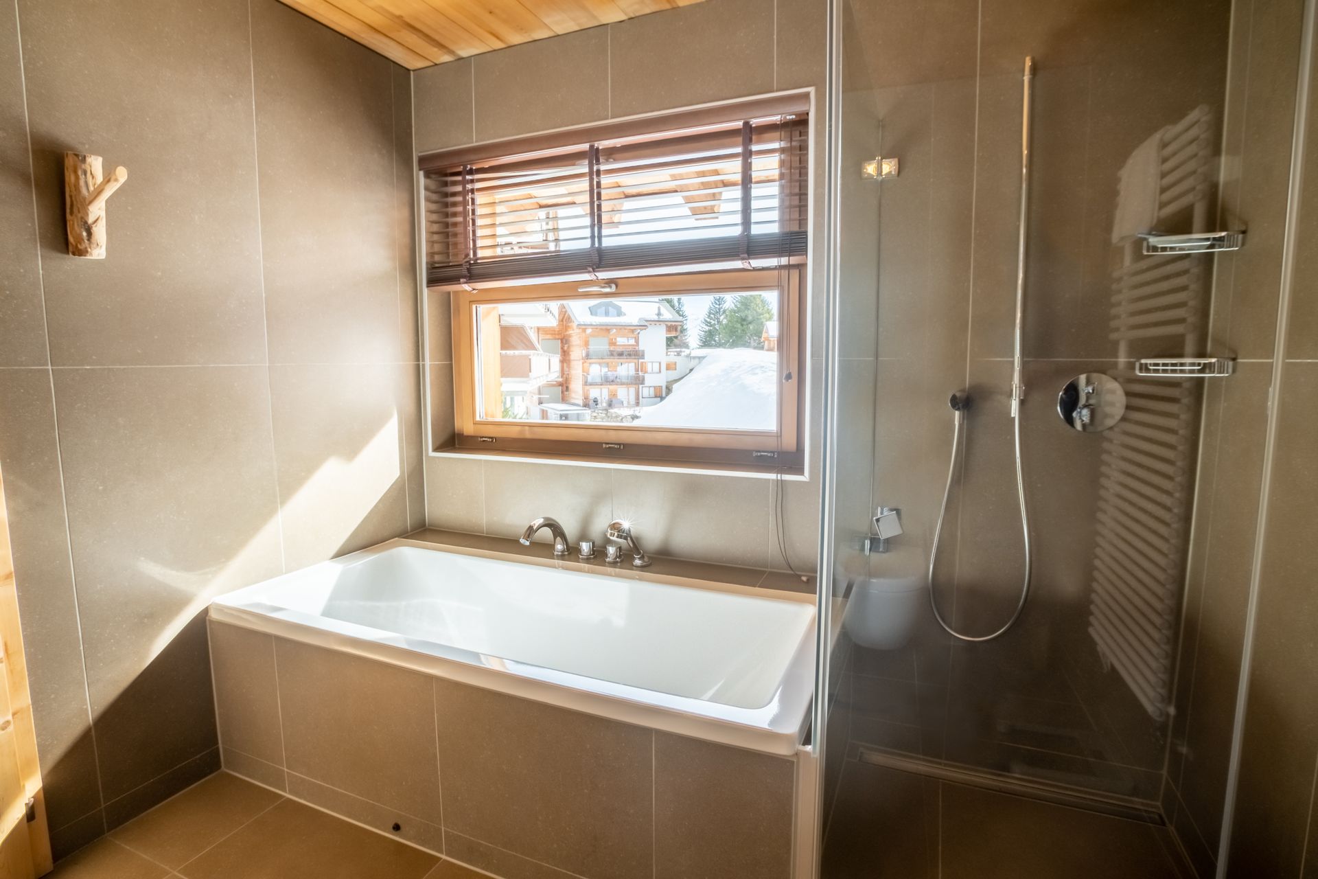 Badezimmer mit Badewanne, Fenster und Dusche; neutrale Farbtöne mit Holzelementen und natürlichem Licht.