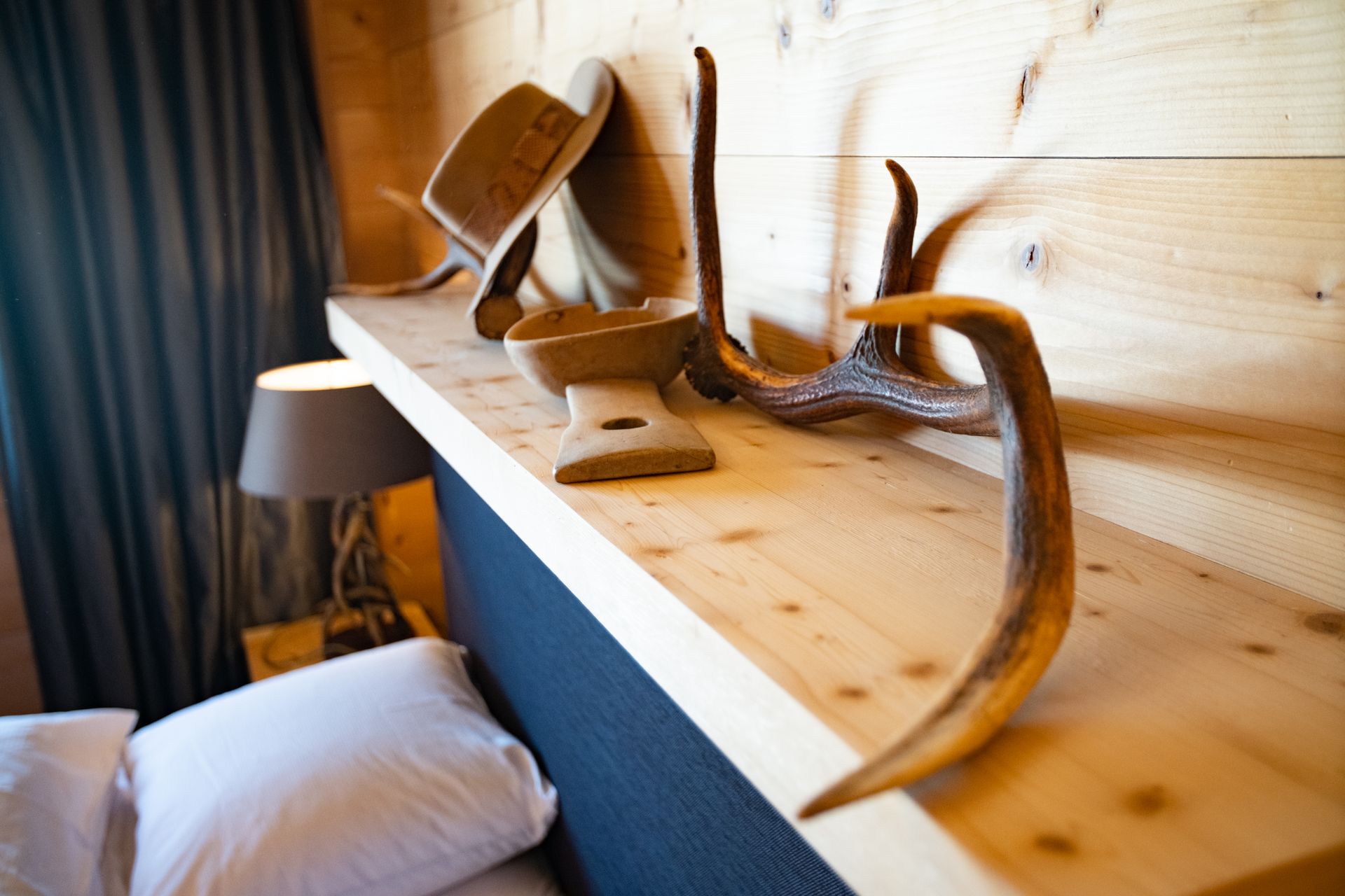 Holzregal mit dekorativem Hut, geschnitztem Objekt und Geweih über einem Bett.