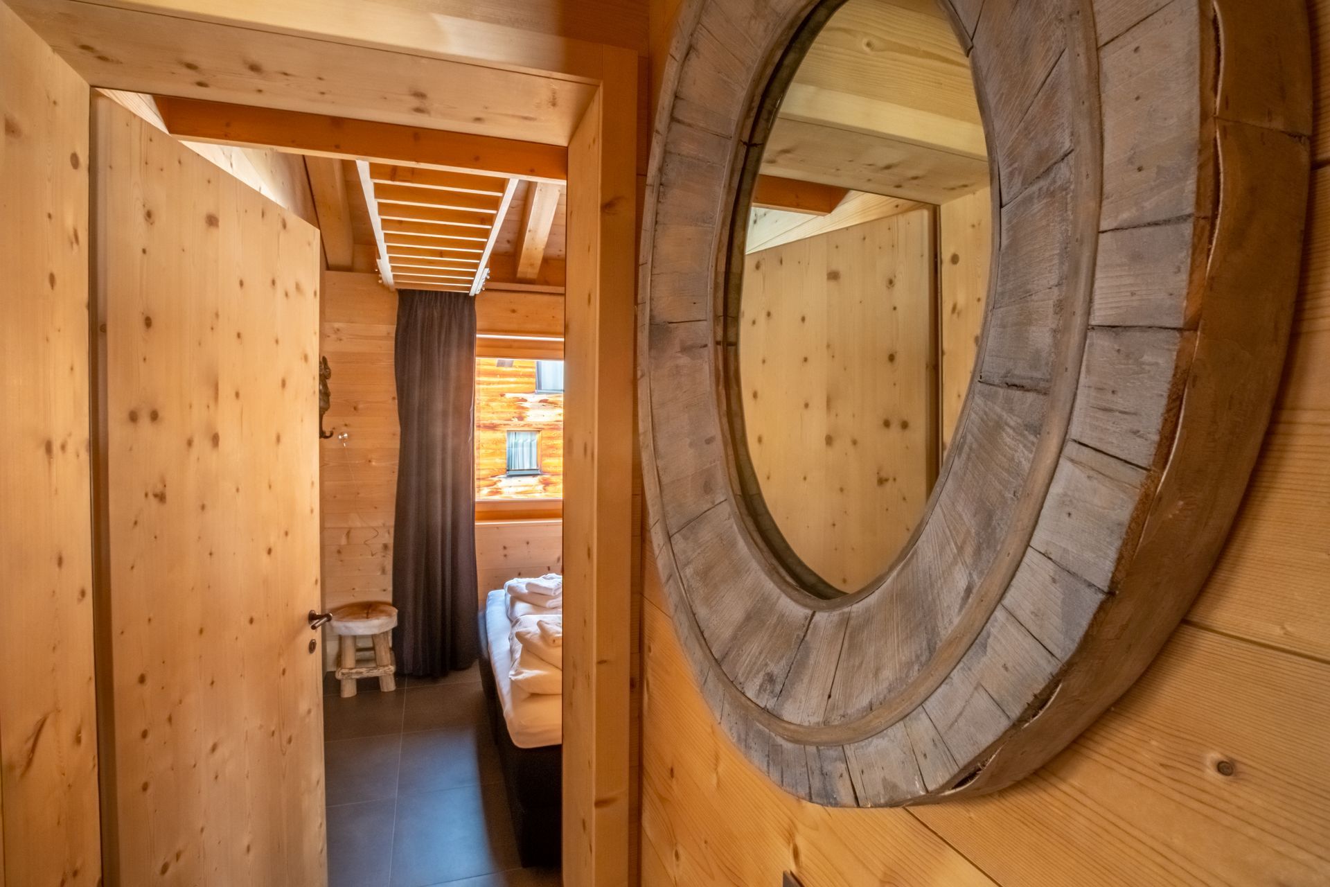 Der Raum ist holzgetäfelt und verfügt über eine Tür, einen Spiegel und ein Bett. Natürliches Licht fällt durch ein Fenster.