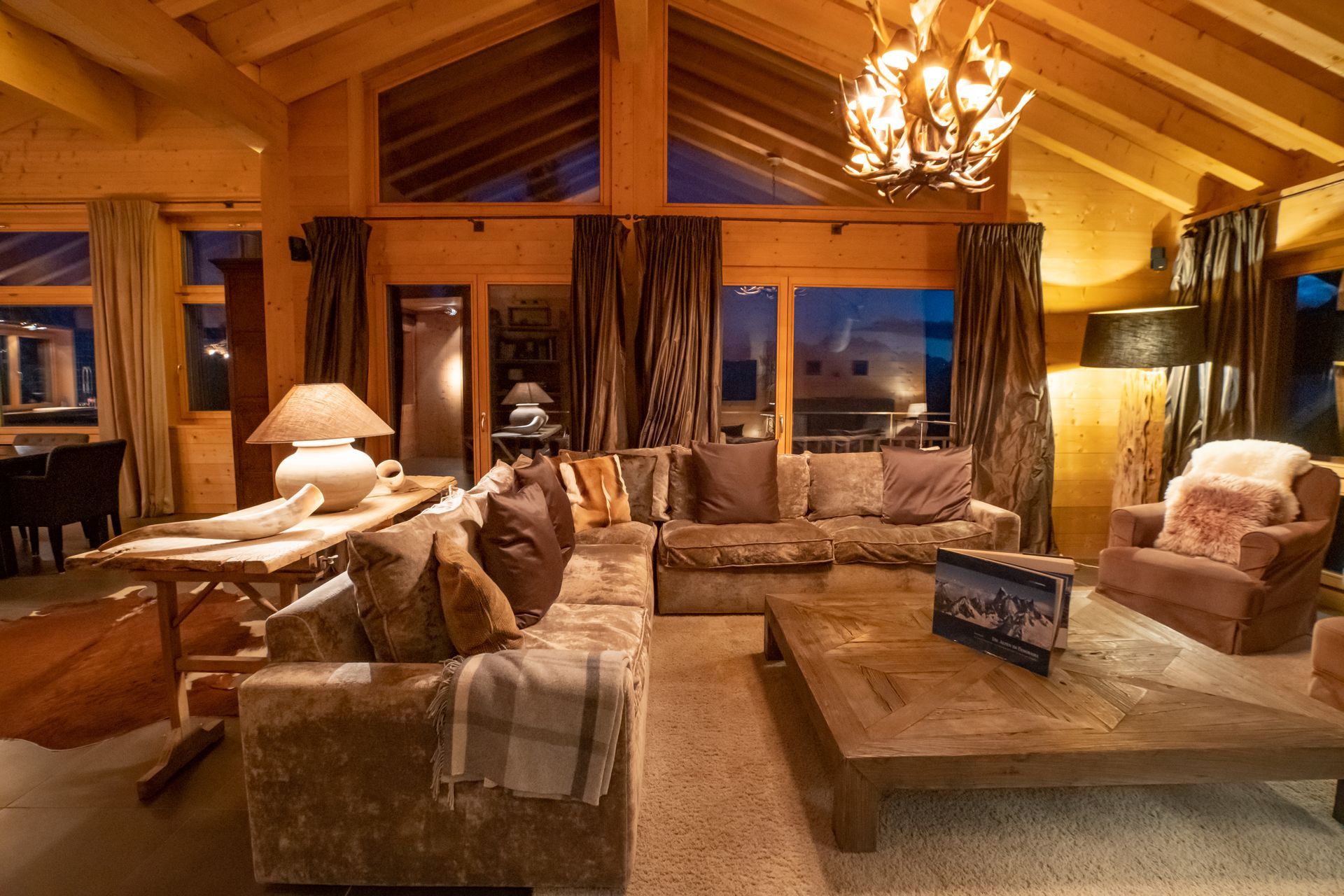 Gemütliches Wohnzimmer im Chalet-Stil aus Holz mit plüschigen Sofas, großen Fenstern und einem rustikalen Kronleuchter.