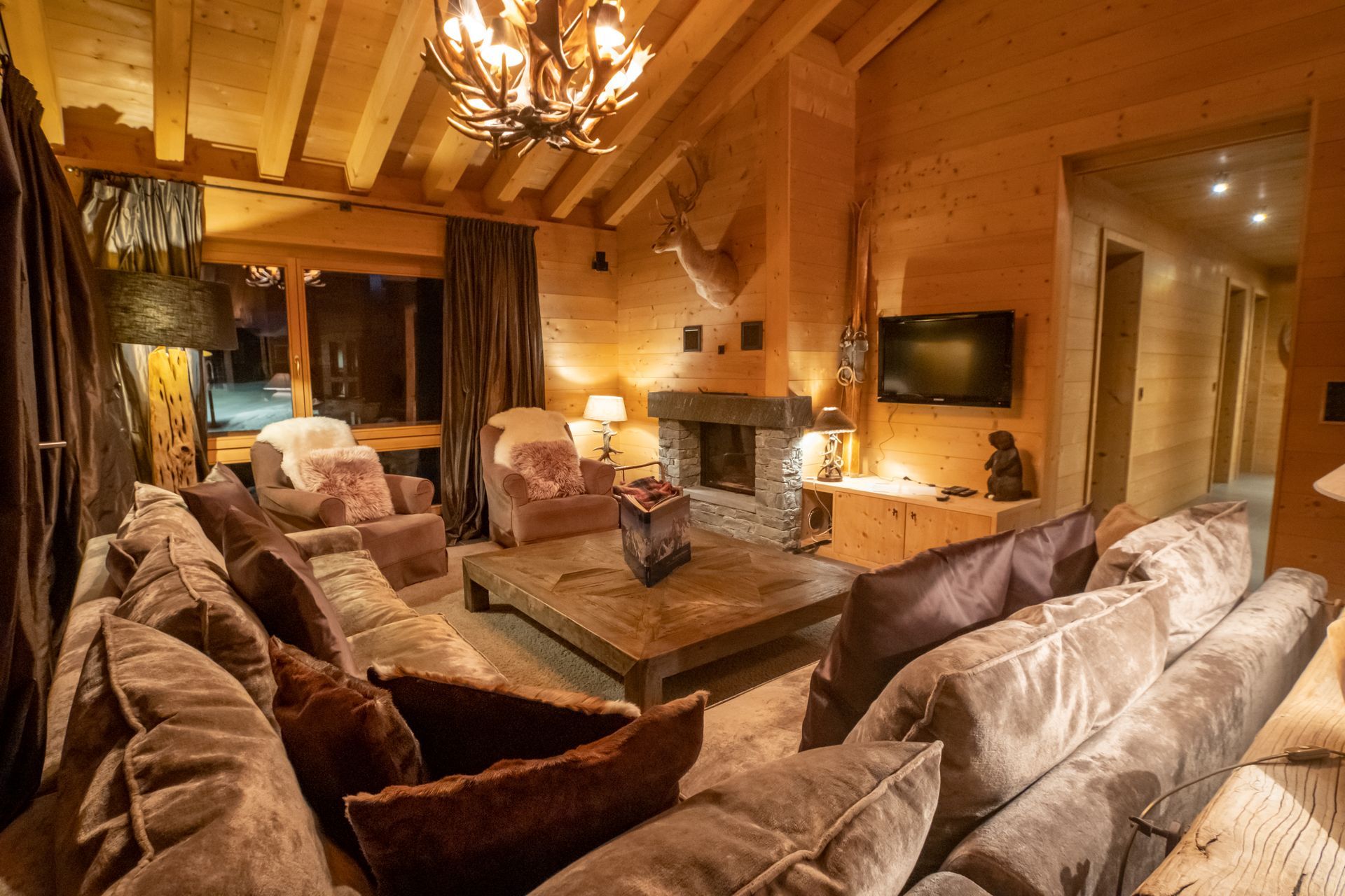 Gemütliches Wohnzimmer mit Holzvertäfelung, Kamin und bequemen braunen Sofas. Warmes Licht sorgt für angenehmes Licht.