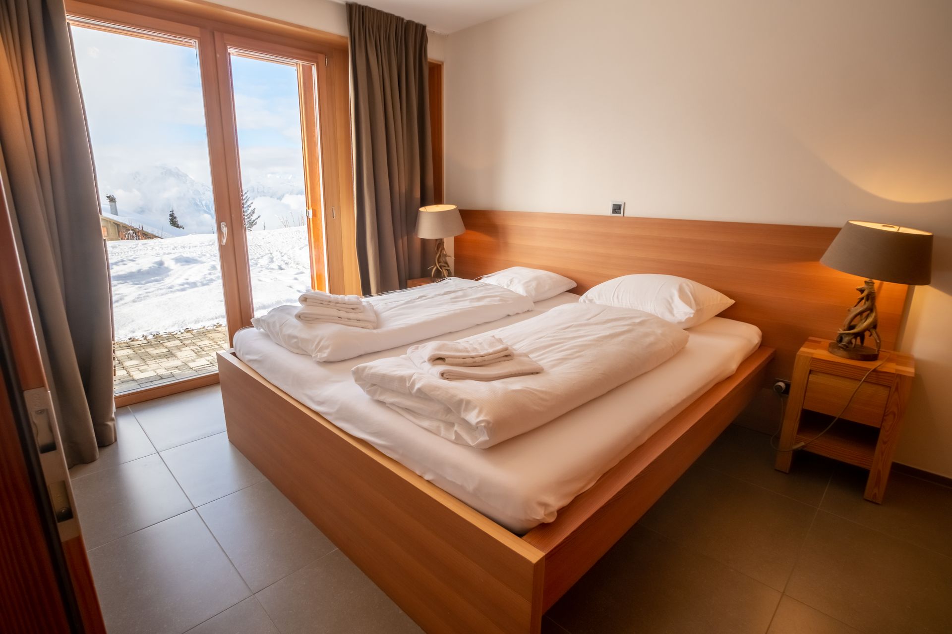 Schlafzimmer mit Doppelbett, Nachttischen und Blick vom schneebedeckten Balkon.