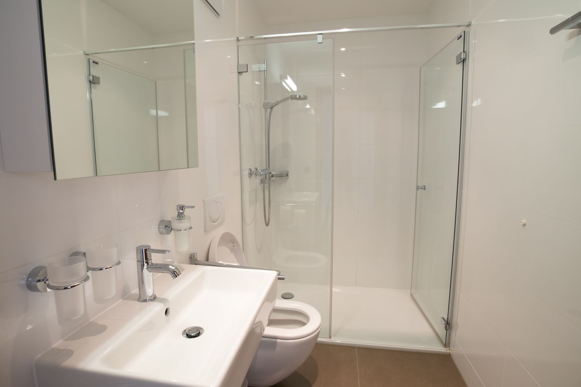 Helles, weißes Badezimmer mit Glasdusche, Toilette und Waschbecken.