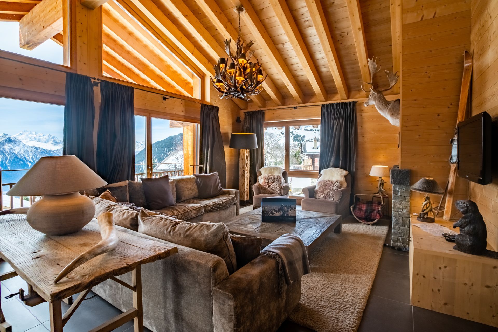Gemütliches Wohnzimmer im Stil einer Holzhütte mit großen Fenstern, Bergblick, edlen Möbeln und Kronleuchter.