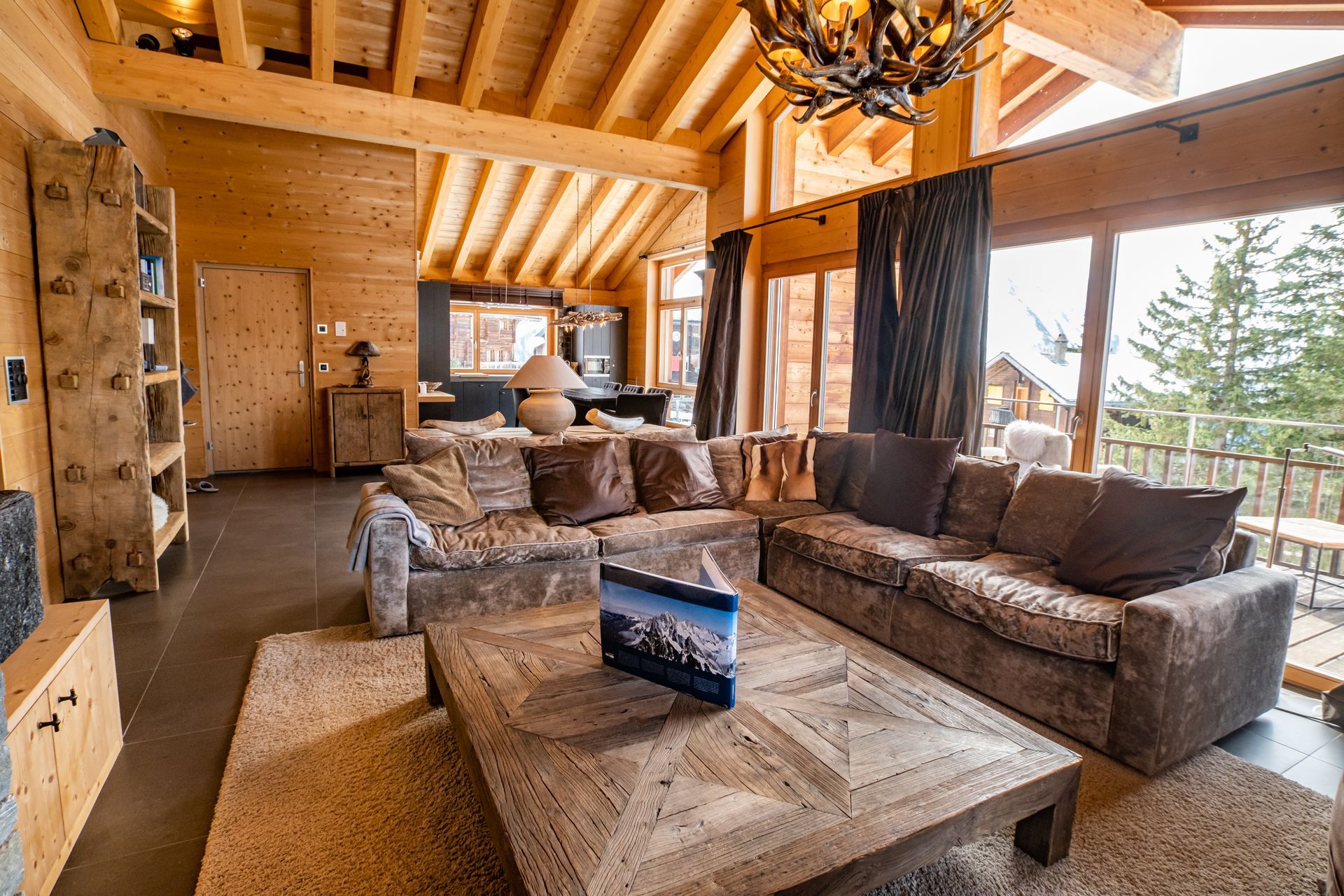 Gemütliches Wohnzimmer in einer Holzhütte mit Sofas, Couchtisch und großen Fenstern mit malerischer Aussicht.