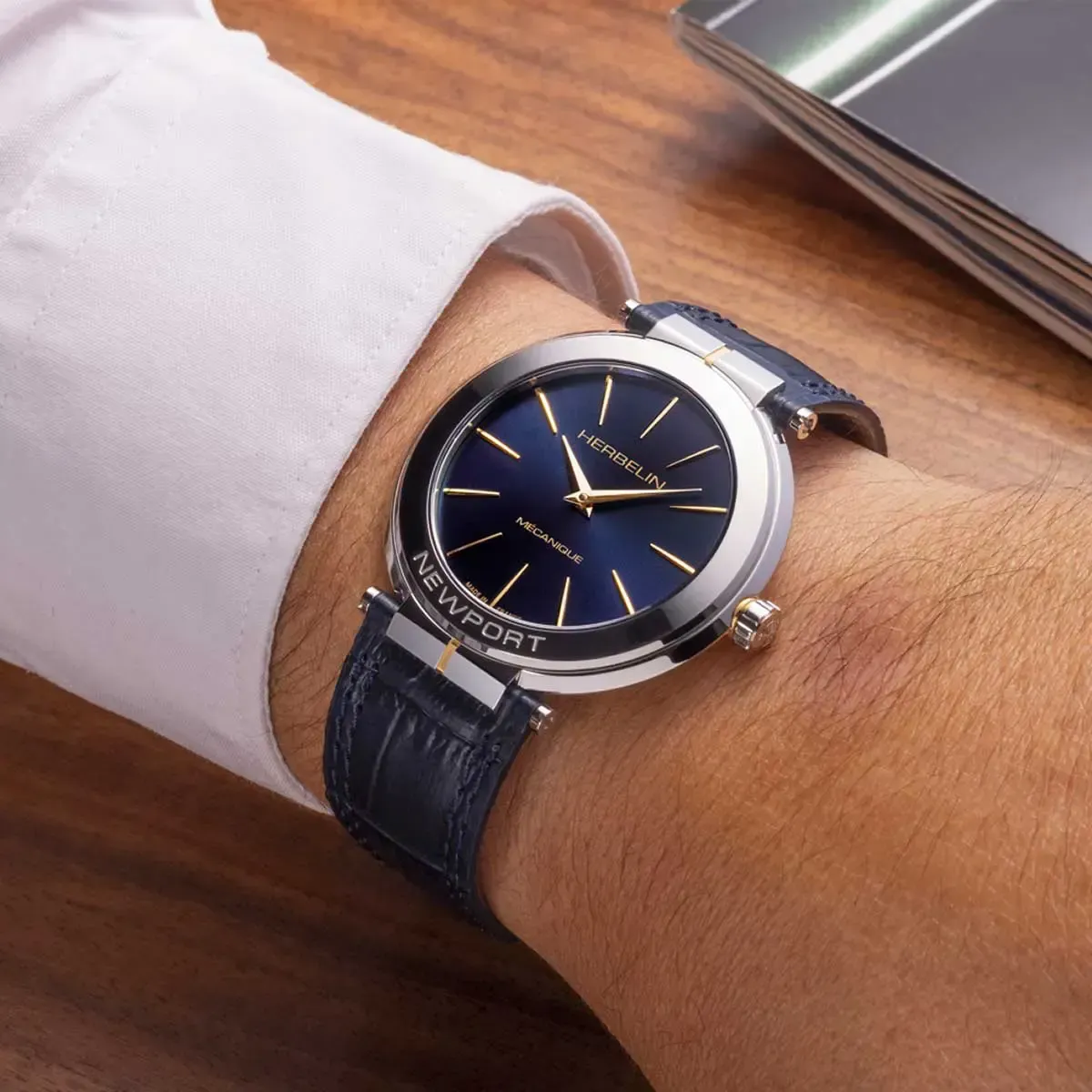 Montre-bracelet avec cadran bleu et accents argentés sur un poignet, à côté d'une manche de chemise blanche sur une surface en bois.
