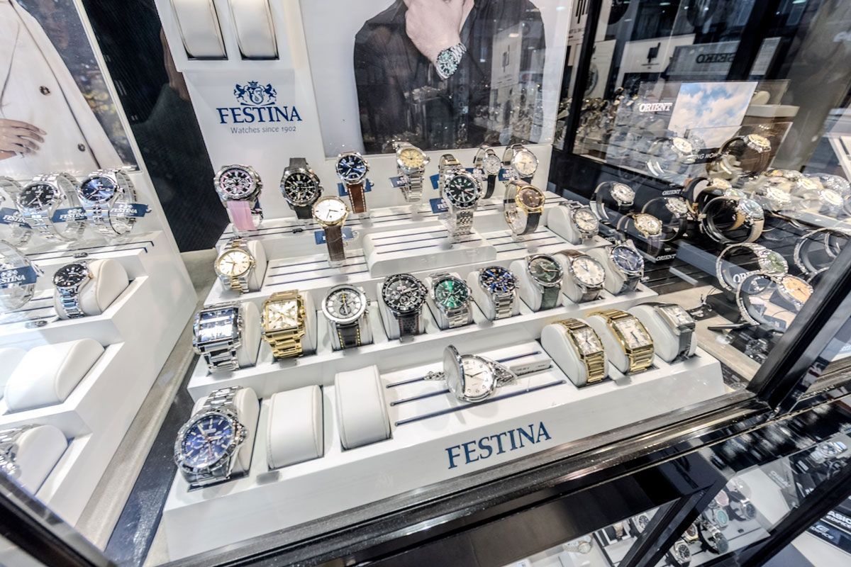 Présentoir de montres Festina dans une vitrine, avec plusieurs montres-bracelets sur des supports blancs.
