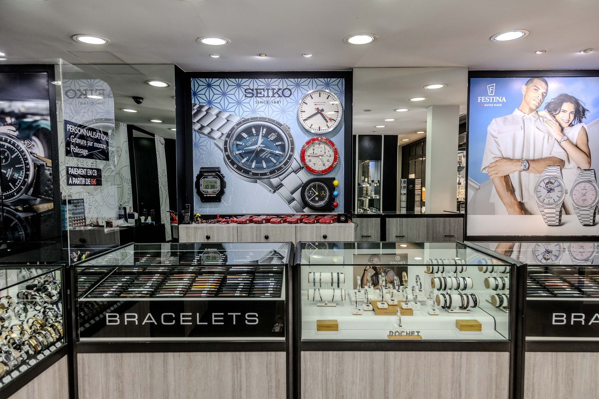 Vitrines de bijouterie présentant des bracelets, avec une grande affiche de montres sur le mur du fond.