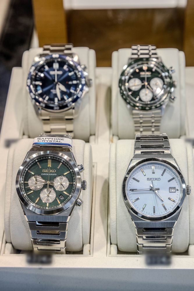 Quatre montres-bracelets présentées dans un écrin à bijoux, avec des cadrans bleu foncé, vert, noir et bleu clair.