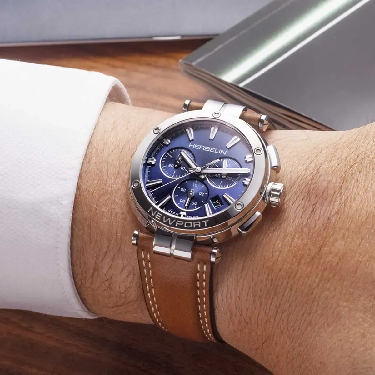 Poignet d'homme avec une montre à cadran bleu, boîtier argenté et bracelet en cuir marron, posée sur une surface en bois.